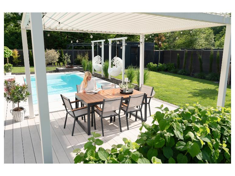Femme lisant à une table à manger sur une terrasse au bord de la piscine avec pergola.