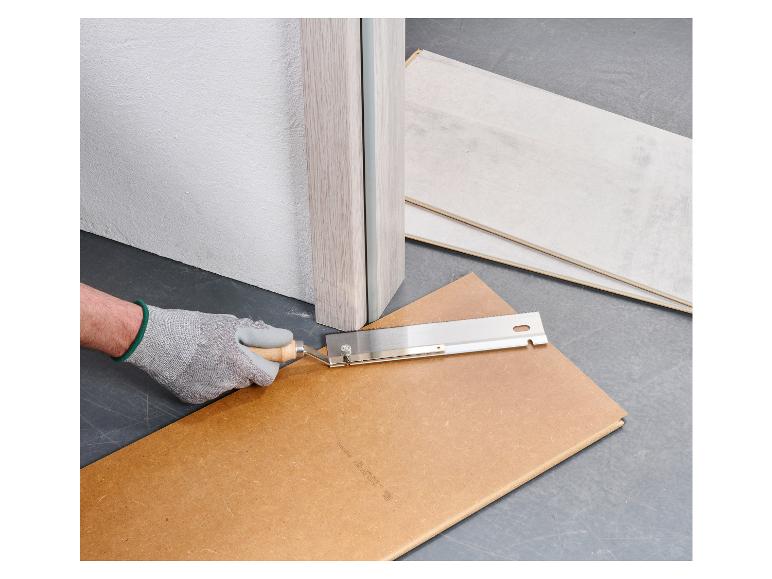 Une main gantée utilise une scie pour couper une planche de bois.