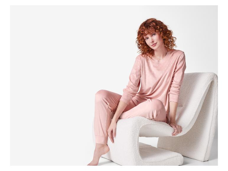 Femme rousse en pyjama rose assise sur une chaise blanche.