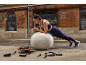 Femme faisant la planche sur un ballon de fitness, avec des bandes de résistance au premier plan.