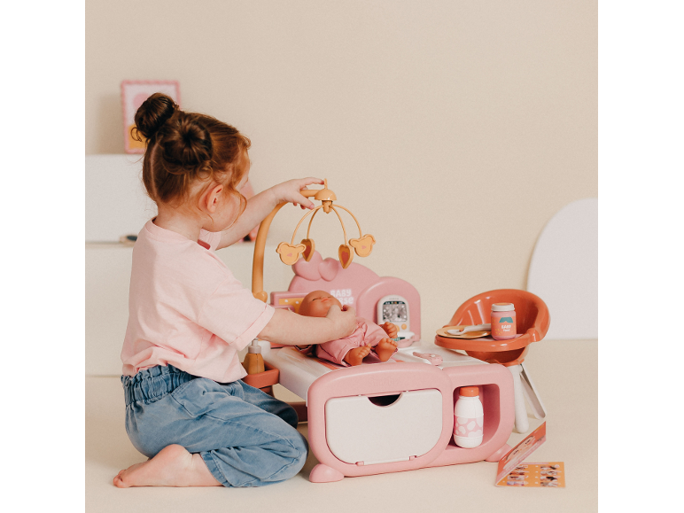 Fille jouant avec un ensemble de soins pour poupée rose, avec berceau et chaise haute.
