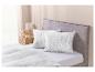 Un lit avec une tête de lit grise, des draps blancs et des oreillers avec un motif géométrique.