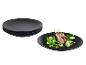 Assiettes noires empilées et une assiette noire avec côtelettes d'agneau et légumes.