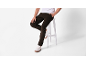 Homme en pantalon de velours côtelé marron et baskets blanches, assis sur un tabouret blanc.