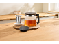 Théière en verre avec du thé et une passoire à thé sur une table en bois.