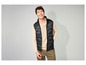 Un homme porte une veste sans manches noire et un pull beige.