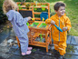 Deux enfants jouent avec de l'eau et du sable dans une cuisine en bois pour enfants.