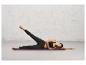 Une femme allongée sur un tapis de yoga violet, vêtue d'un legging noir et d'un soutien-gorge de sport.