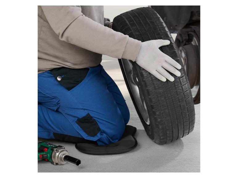 Personne en salopette bleue et gants changeant un pneu, avec des outils au sol.