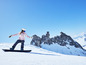 Une snowboardeuse en tenue rose et lunettes bleues, descend une pente enneigée en snowboard.