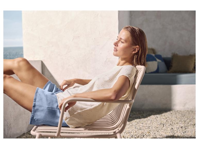 Femme se relaxant dans un fauteuil extérieur, portant un haut brodé et un short.