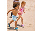 Deux enfants courent sur la plage, un garçon en short de bain et une fille en maillot de bain à imprimé flamant rose.