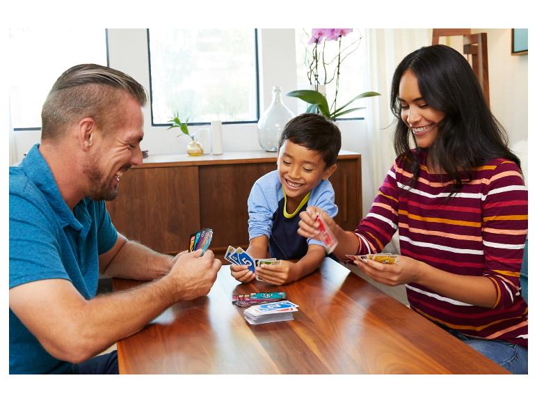 Famille jouant aux cartes UNO à une table en bois, riant et souriant.