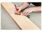 Une main utilise une règle et un crayon pour tracer une ligne sur une planche de bois.