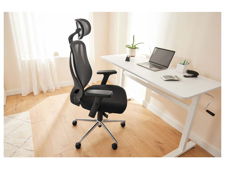 Un fauteuil de bureau noir avec un dossier en maille à côté d'un bureau blanc avec un ordinateur portable et des fournitures de bureau.