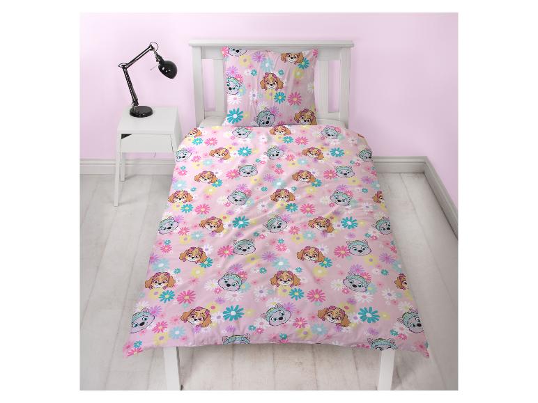 Parure de lit enfant rose avec motifs de chiens et de fleurs sur un lit à cadre blanc.