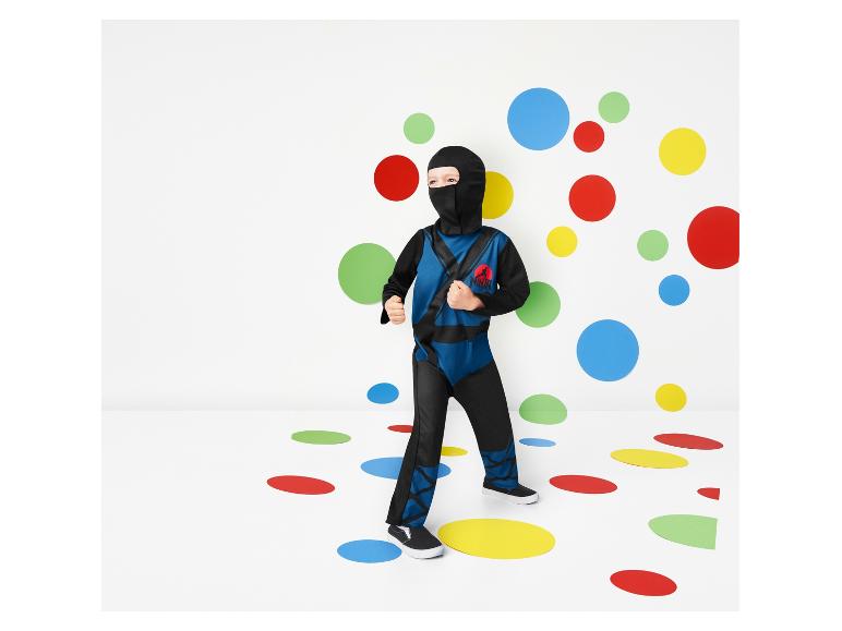 Un enfant en costume de ninja se tient sur un sol avec des points de couleur.
