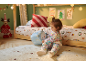 Enfant en pyjama de Noël jouant avec une peluche sur un tapis dans une chambre décorée.
