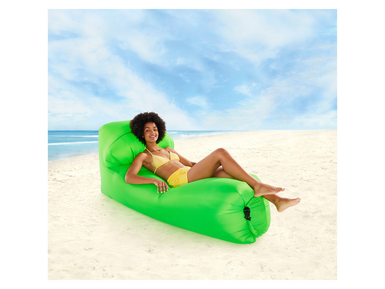 Une femme se relaxe sur une chaise longue gonflable verte à la plage.