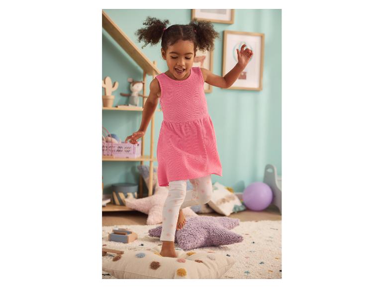 Fillette en robe rose et leggings LUPILU® à motifs sautant sur des coussins.