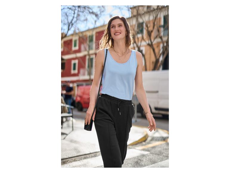 Femme élégante portant un débardeur bleu clair et un pantalon de jogging noir en ville.