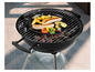 Un barbecue rond noir avec une grille et un plateau avec des saucisses, des pommes de terre et des courgettes.