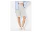 Femme en short gris clair, crop top blanc, chemise rayée bleue et baskets blanches.