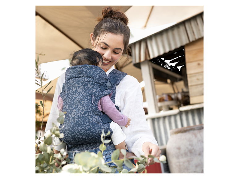 Une maman porte son bébé dans un porte-bébé Infantino à motif floral.