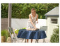 Une femme posant une nappe bleue sur une table de jardin.