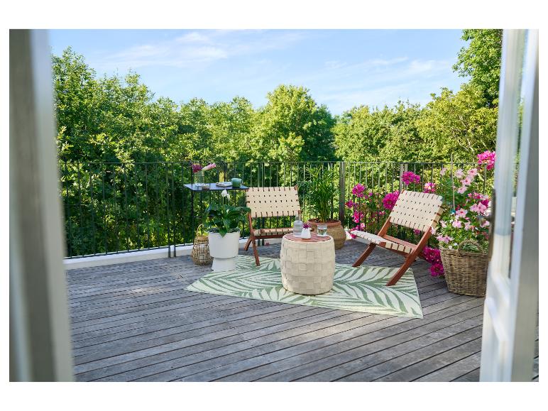 Balcon avec chaises pliantes, table d'appoint, plantes et tapis à motifs de feuilles.