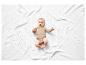 Un bébé dans une combinaison beige est allongé sur une couverture blanche en tricot.