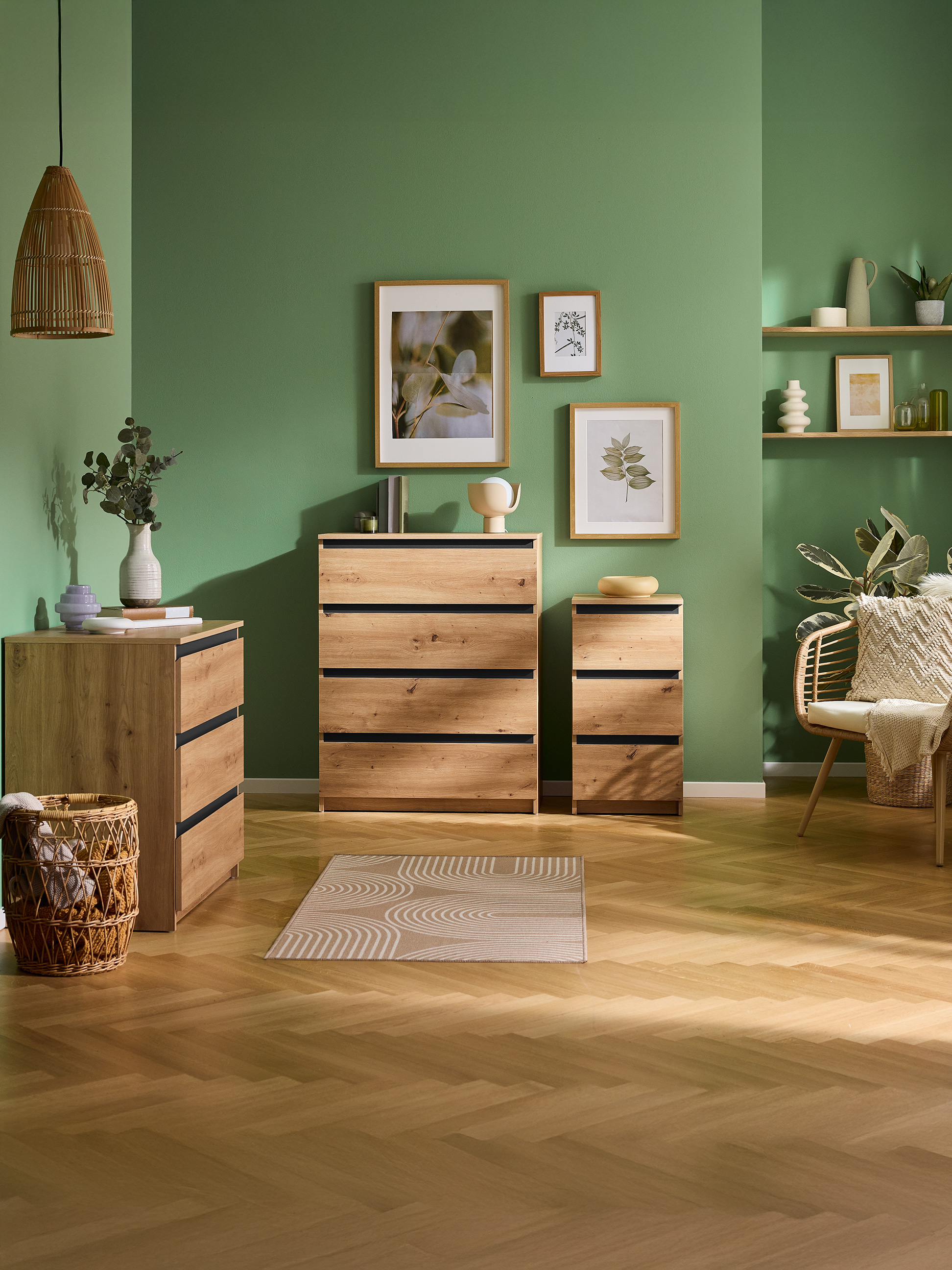 Pièce verte avec commodes en bois, étagères et fauteuil en osier, avec art botanique.