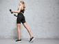 Femme en leggings noirs et soutien-gorge de sport s'entraînant avec des haltères.