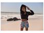 Femme en sportswear sur la plage : veste, top et shorts imprimés.