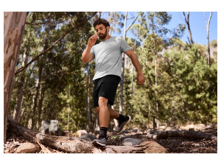 Homme en t-shirt gris et short noir faisant du trail en forêt.