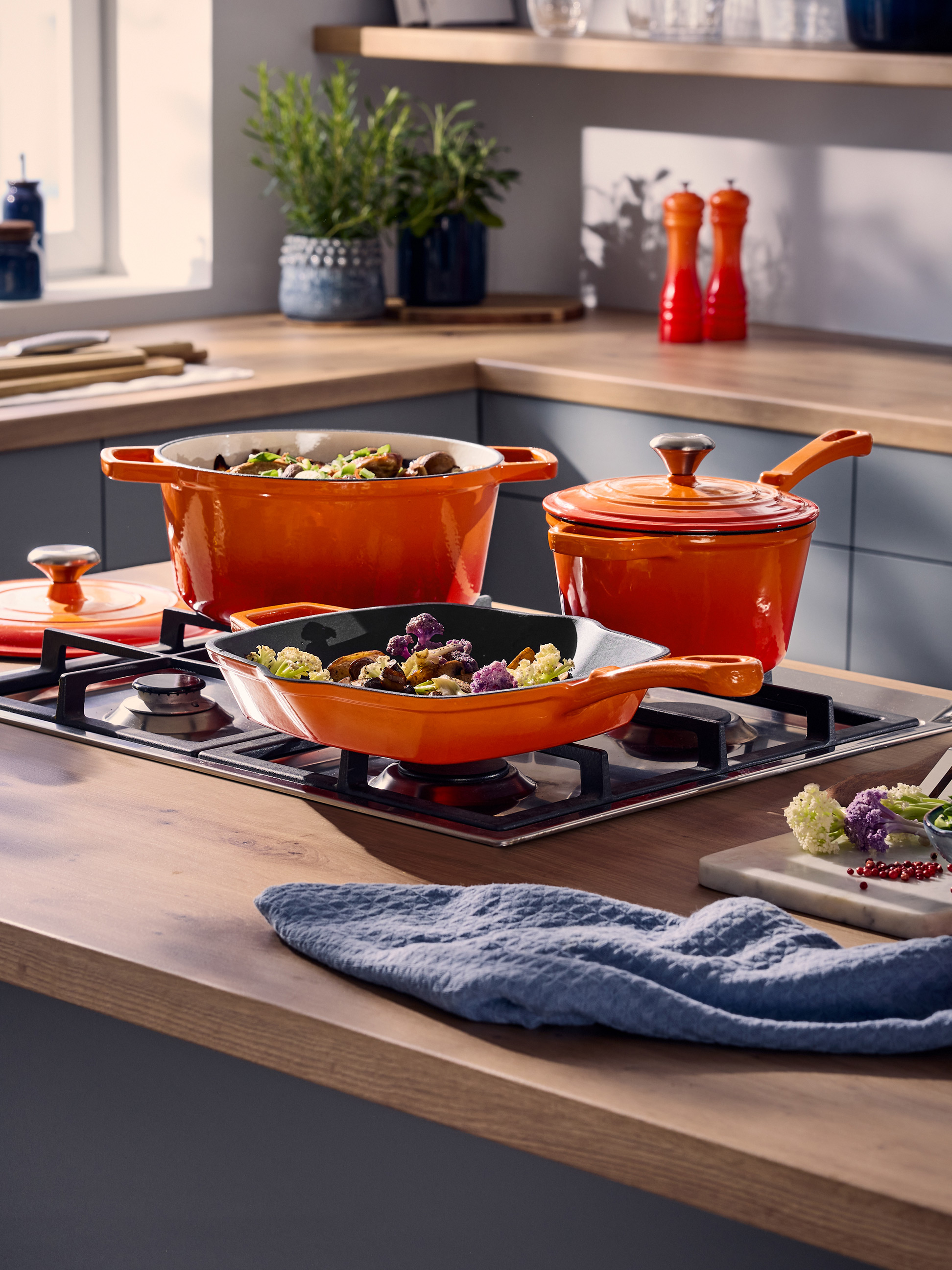 Casseroles et poêles orange sur une cuisinière à gaz dans une cuisine moderne.