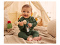 Un bébé dans une tenue verte, avec un hochet en bois, assis sur une couverture tricotée.