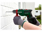 Une personne utilise une perceuse Parkside verte pour percer un trou dans un mur en briques blanches.