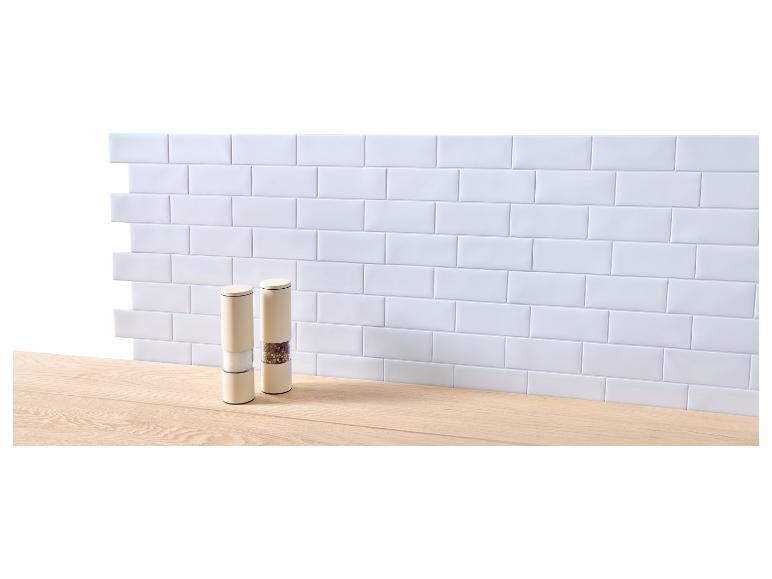 Deux moulins à sel et à poivre sur un plan de travail en bois devant un mur carrelé blanc.