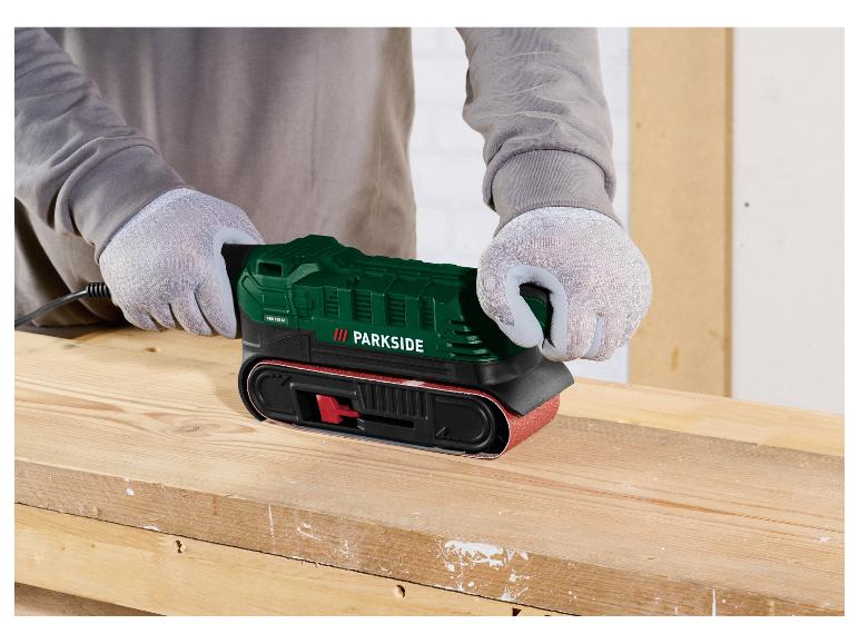 Personne gantée ponce du bois avec une ponceuse à bande verte Parkside.