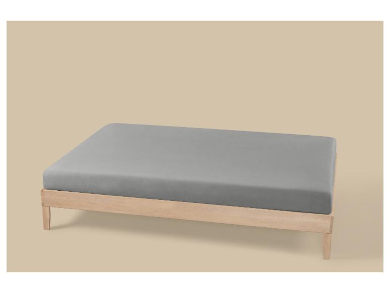 Lit en bois avec matelas gris sur fond beige.