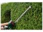 Une personne utilisant une taille-haie verte pour tailler un buisson.