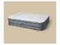 Matelas gonflable gris et blanc avec oreiller intégré sur fond beige.