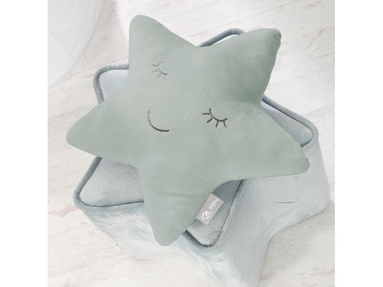 Coussin en forme d'étoile vert menthe avec des yeux et une bouche brodés, posé sur un panier de rangement assorti.
