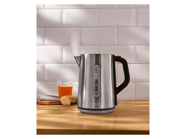 Bouilloire en acier inoxydable avec de la vapeur, à côté d'une tasse de thé et de biscuits.