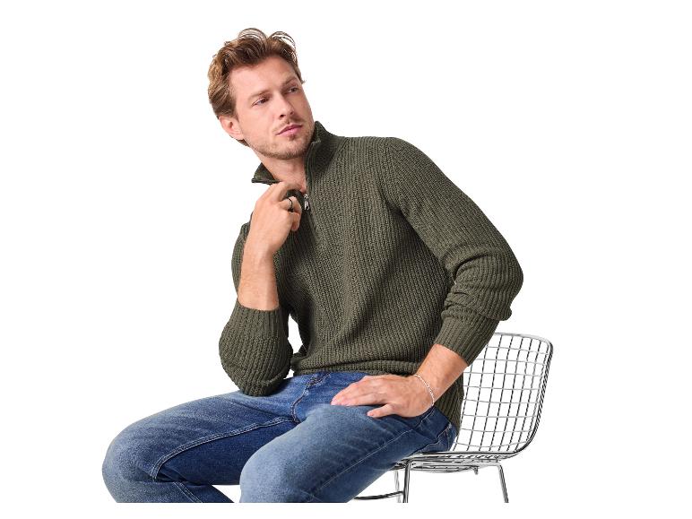 Homme en pull tricoté vert foncé à demi-zip et jean bleu, assis sur une chaise.