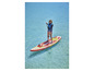 Une femme pagaye sur un paddleboard gonflable rouge et jaune de la marque Mistral.