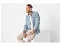Homme en chemise bleue et pantalon beige, assis sur un cube blanc.