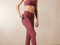 Une femme porte un soutien-gorge de sport rose et un legging avec un téléphone dans la poche.