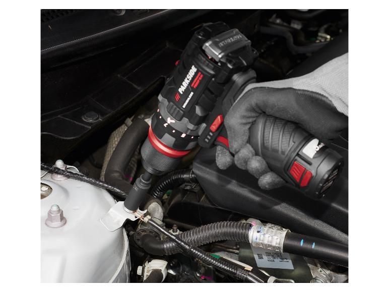 Un tournevis sans fil Parkside est utilisé pour serrer une vis dans le moteur d'une voiture.